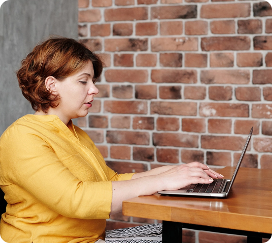 Close Up Picture of Woman in Yellow Crew Neck T-shirt Sitting on Desk Typing on her Laptop