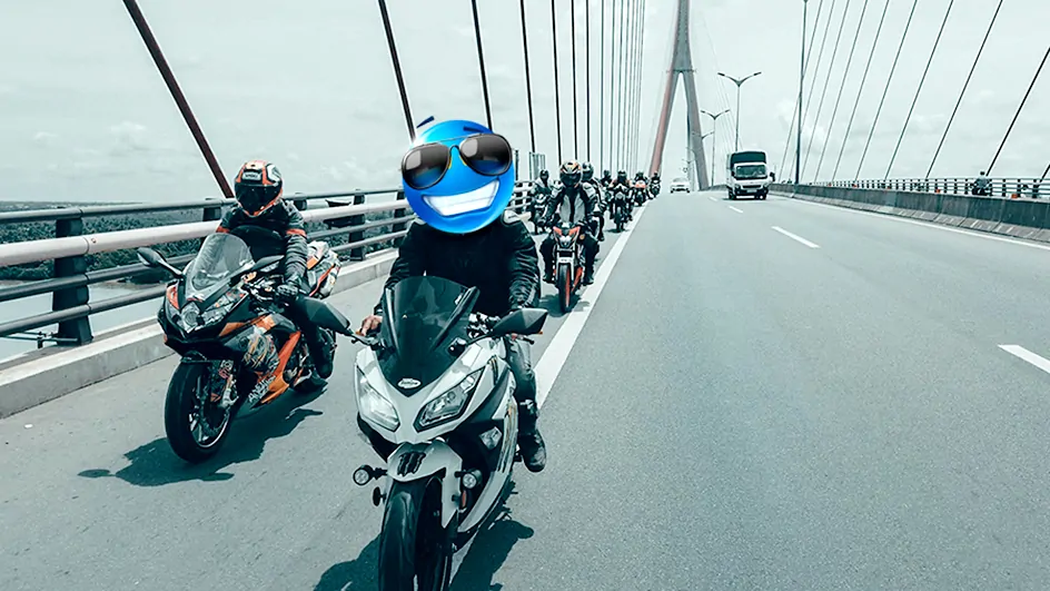 A group of motorcyclists riding in formation across a suspension bridge.