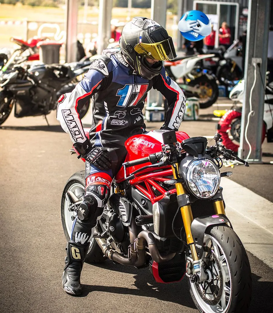 A rider in full leathers sits on a Ducati Monster in the pit lane, preparing for a track session.