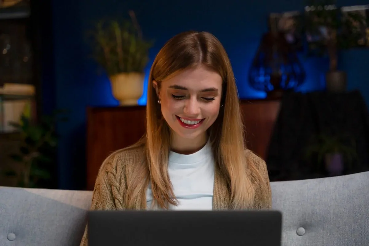 A woman smiles while using a laptop at home, taking part in an online research session.