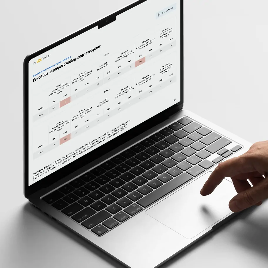 A hand interacts with a laptop trackpad displaying a Greek-language data table titled "Ease and confidence in completing the purchase," comparing metrics like SEQ and CSAT across multiple usability test rounds, with one cell highlighted in red.