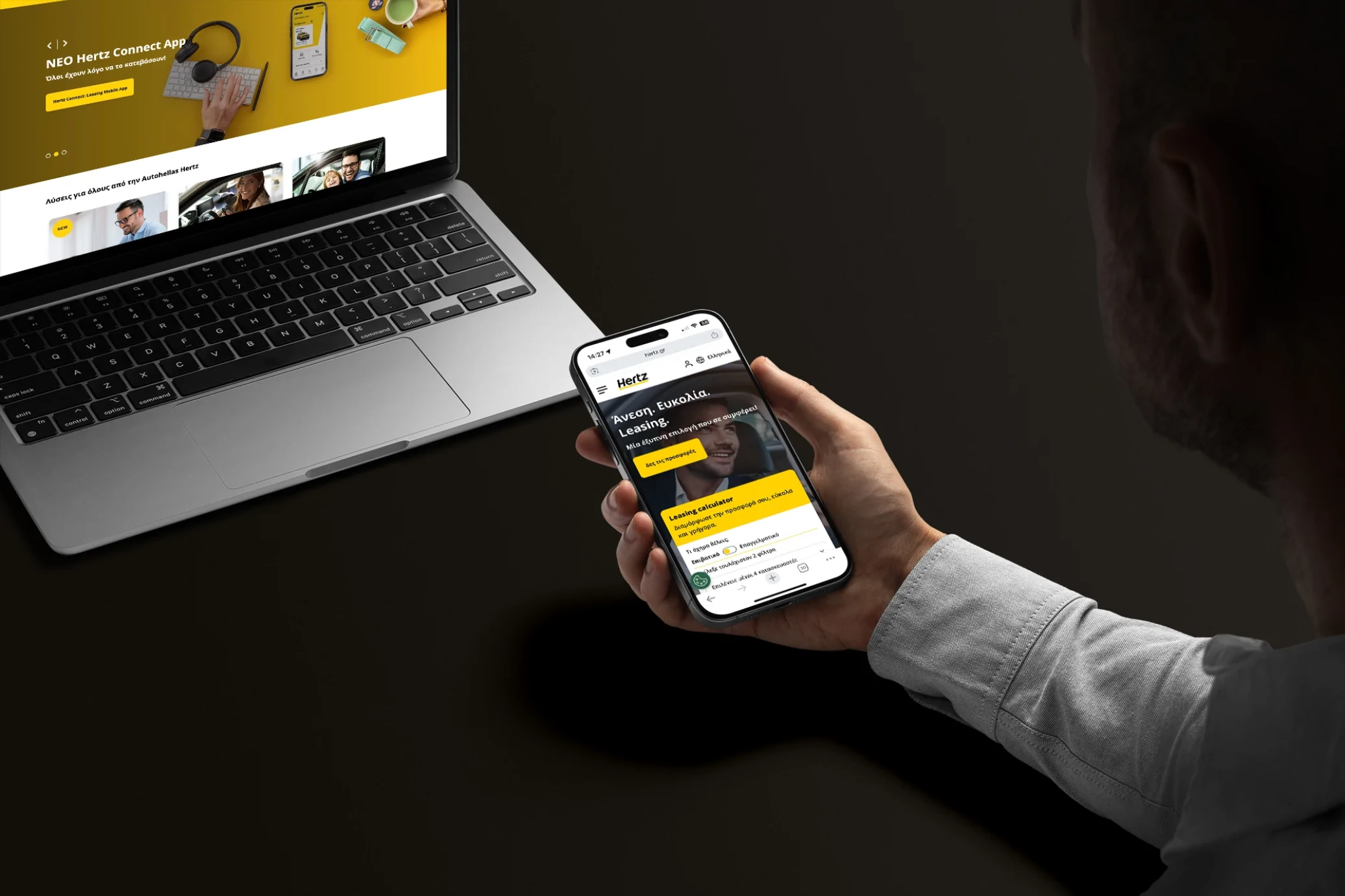 A person holds a smartphone displaying a website, with a laptop open in the background showing the same site — illustrating a responsive digital product across devices.