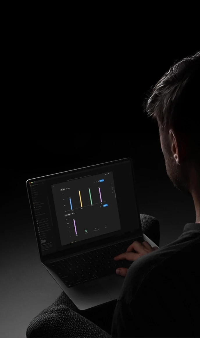 A person viewed from behind works on a laptop displaying a dark-themed data dashboard with colorful bar charts.