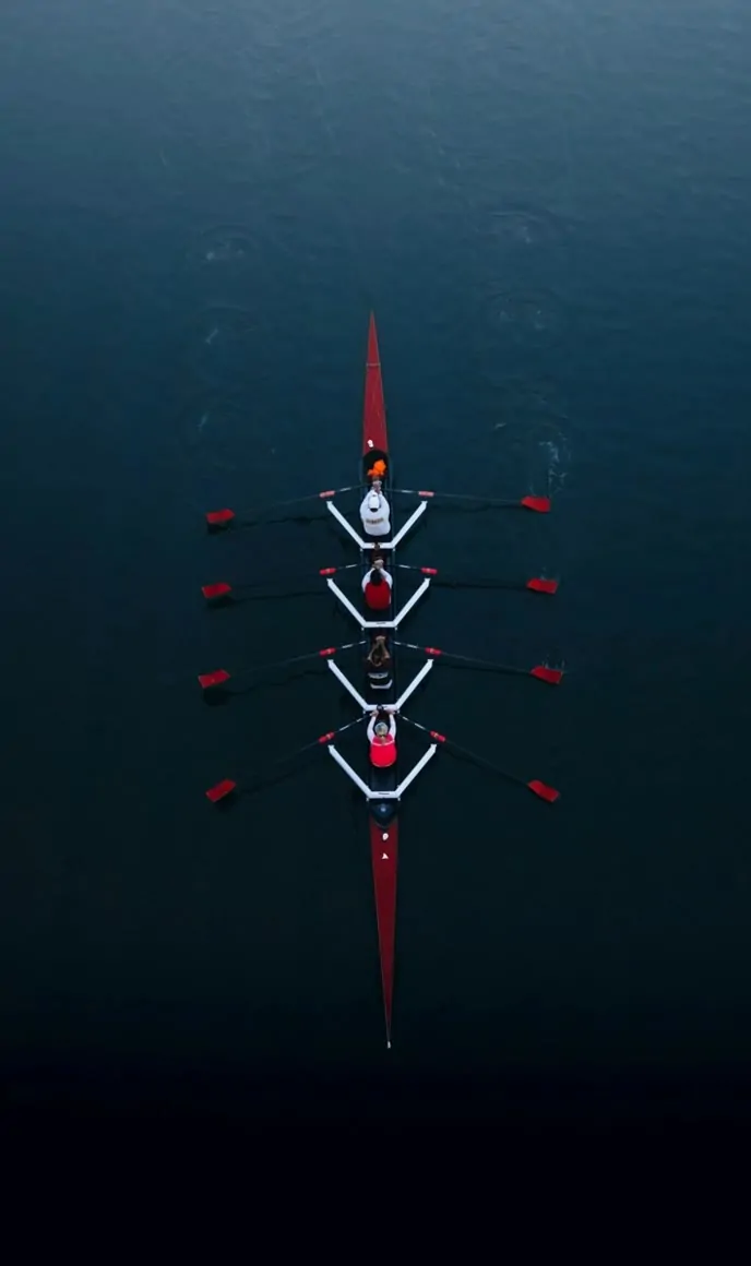Aerial view of a four-person rowing team moving in perfect sync on dark water.